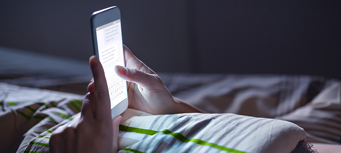 Dem blauen Licht auf der Spur Frau liegt im Bett und schaut auf ihr Smartphone